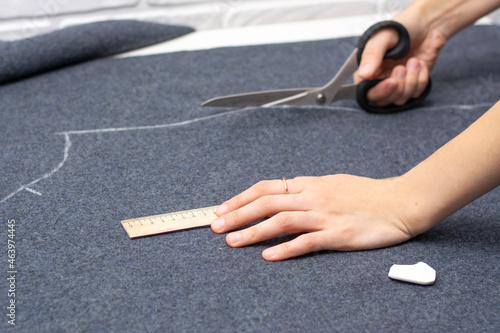 A ruler is in women's hands. The right hand cuts out a piece of gray drape fabric. Sewing a coat.