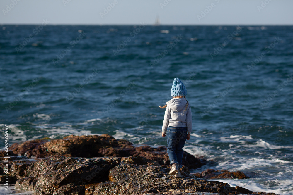 Happy pretty girl walks along the sea coast against the background of the sea, from behind a beautiful landscape