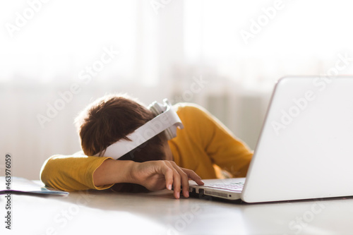 Fotografie tired schoolboy sleeps with his head on a table in front of a laptop