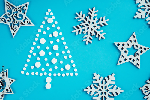 White round pills, laid out in shape of Christmas tree with wooden snowflakes on light blue background, flat lay