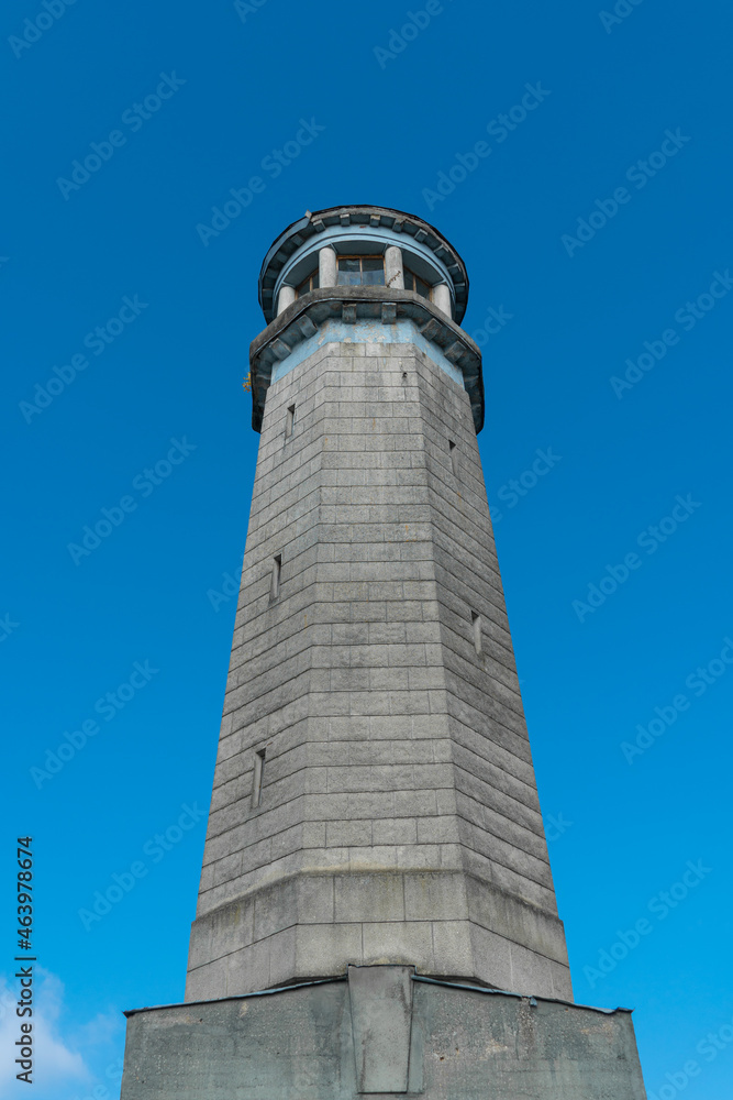 The old stone building of the lighthouse rises against the blue sky, vertical photo