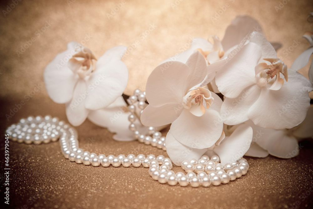 white Orchid and pearl necklace on a shiny gold background
