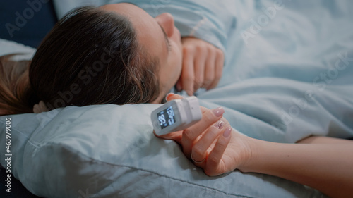 Close up of oximeter on hand of sick woman with disease resting. Adult with medical instrument measuring oxygen saturation and pulse pressure, feeling ill and having coronavirus symptoms