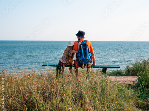 Happy father and daughter sitting on bench on marine landscape back view. Dad and child having fun walking together looking at the sea from above.Lifestyle real people. Happiness family travel concept