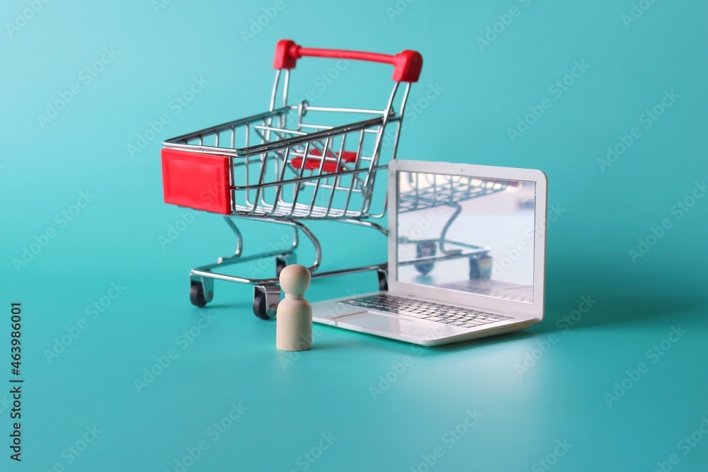 Online shopping concept. Wooden doll in front of laptop and shopping trolley