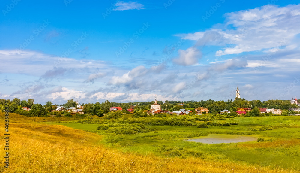 Summer landscape with buildings, churches, trees, shrubs, grass, sky with clouds of the city of Suzdal in Russia