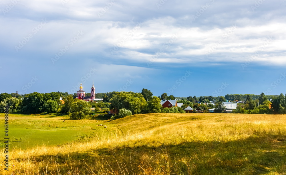Obraz premium Summer landscape with buildings, churches, trees, shrubs, grass, sky with clouds of the city of Suzdal in Russia