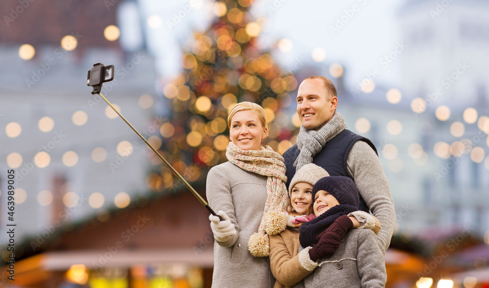 winter holidays, technology and people concept - happy family taking picture with smartphone and selfie stick over christmas market background winter holidays, technology and people concept - happy family taking picture with smartphone and selfie stick over christmas market background