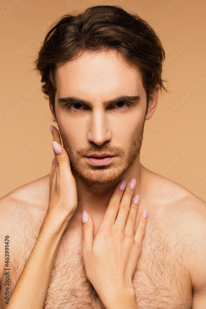 Obraz premium sexy man looking at camera near hands of woman seducing him isolated on beige.