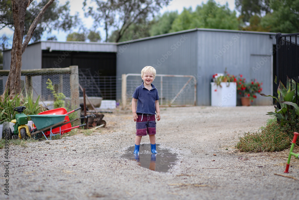 Little boy wearing gum boots jumping and splashing in puddle Little boy wearing gum boots jumping and splashing in puddle