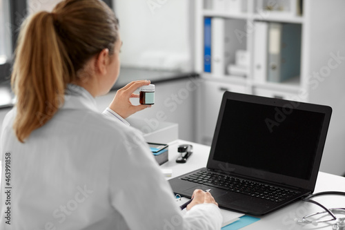 healthcare, technology and medicine concept - female doctor in white coat with laptop computer and drugs having video call at hospital