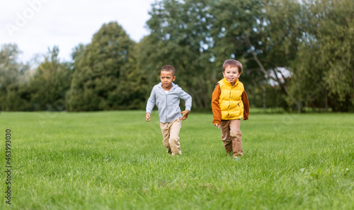 childhood, leisure and people concept - happy little boys running on green field at park