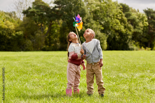childhood, leisure and people concept - happy kids with pinwheel having fun at park