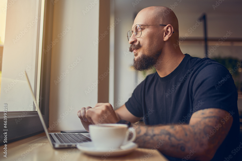 Focused hipster millennial man works at laptop while sitting in cafe with coffee. Freelance concept Focused hipster millennial man works at laptop while sitting in cafe with coffee. Freelance concept