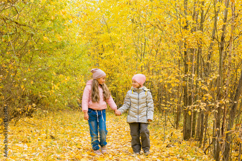 Two girls are walking in an autumn city park on a warm sunny day. Children's friendship.