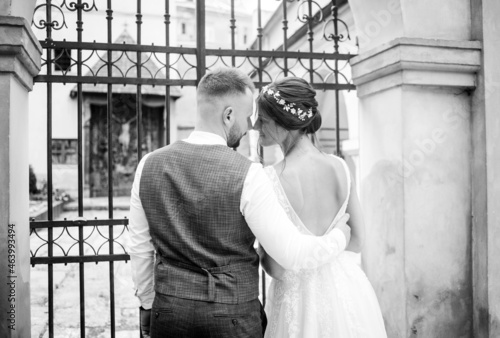 Black and white photo. Sensual couple hugging in front of a wrought iron gate.