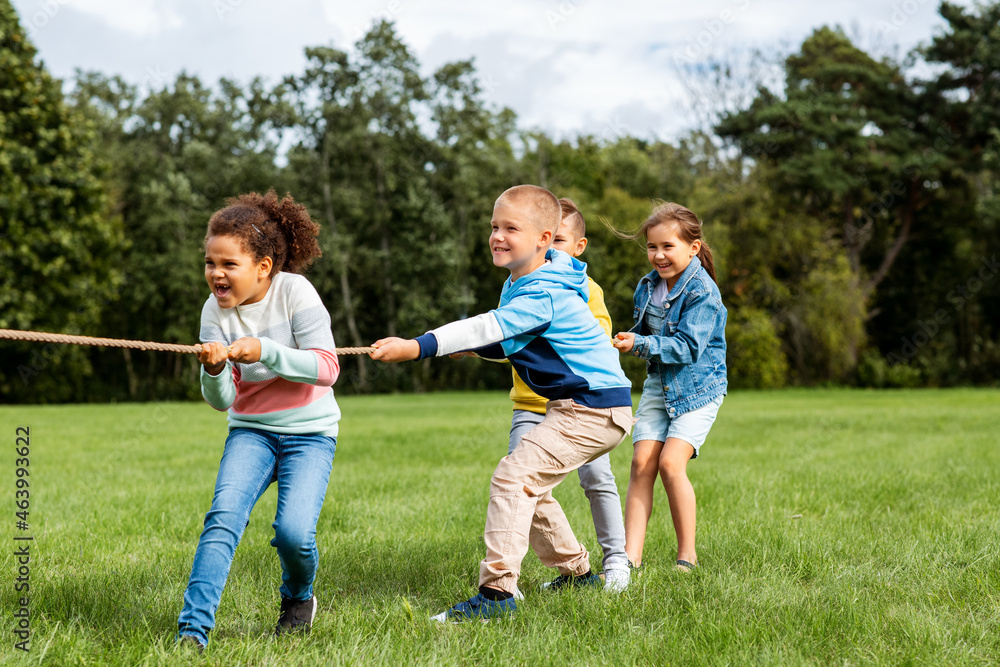 childhood, leisure and people concept - group of happy kids playing tug-of-war game and running at park