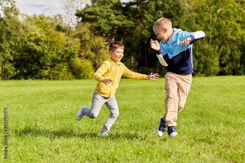 childhood, leisure and people concept - two happy boys playing tag game and running on lawn at park