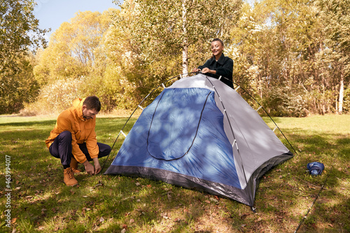 camping  tourism and travel concept - happy couple setting up tent outdoors