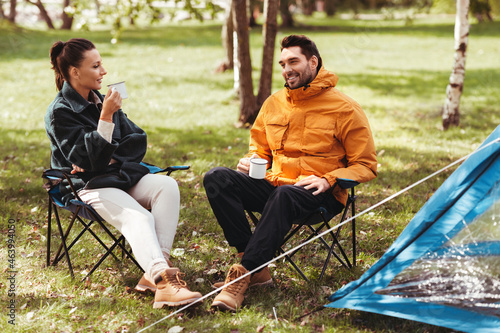 camping, tourism and travel concept - happy couple drinking tea at tent camp #463994050