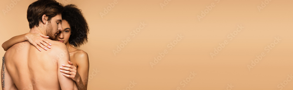 back view of shirtless man near young and sensual latin woman embracing him isolated on beige, banner. back view of shirtless man near young and sensual latin woman embracing him isolated on beige, banner.