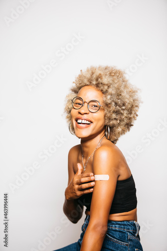 Portrait of a Young black latin woman showing the band-aid on her arm after vaccination standing Against White Background