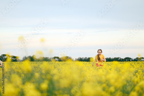 Pretty long haired girl playing in vibrant canola field in full bloom during Spring season