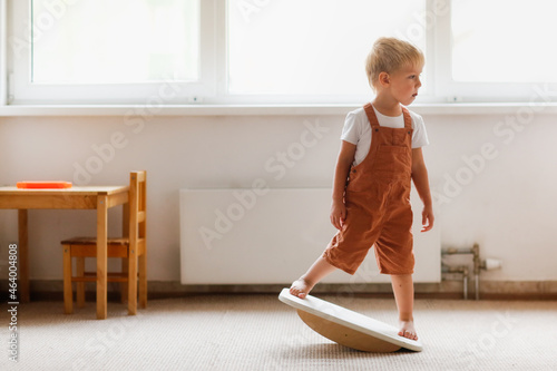 Cute toddler child boy swinging on a balancing board in a light room, physical and sensory development of children photo