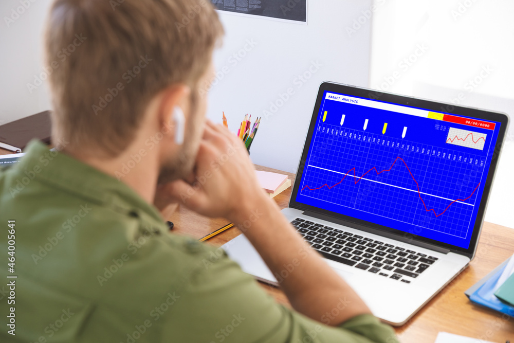 Caucasian businessman sitting at desk using laptop with statistical data on screen Caucasian businessman sitting at desk using laptop with statistical data on screen