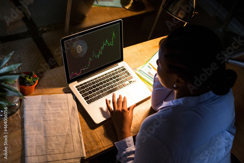 Biracial businesswoman sitting at desk, using laptop with statistical data on screen