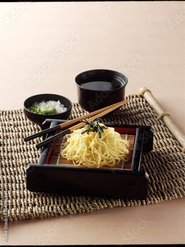 Japanese cold  noodles or Zaru ramen with chopped green onions, grated wasabi and cup for dipping sauce on braided woven rattan jute Placemat on wooden background. photo