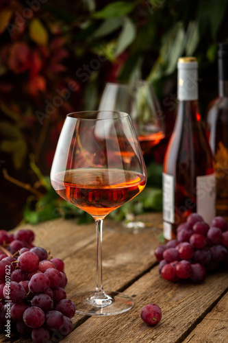 Autumn cozy romantic evening outdoors  wooden table with glasses with rose wine  bottles of wine and grapes