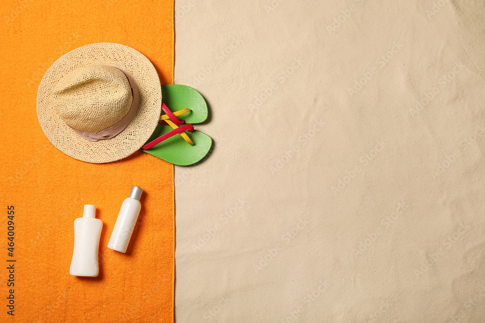 Beach towel, hat, sun protection products and flip flops on sand, flat lay. Space for text
