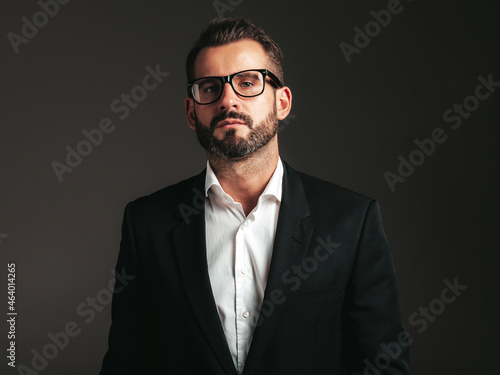 Portrait of handsome confident stylish hipster lambersexual model. Sexy modern man dressed in elegant black suit. Fashion male posing in studio on dark background. In spectacles