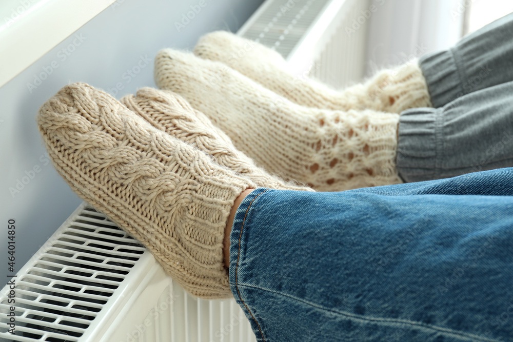 Concept of heating season with legs in knitted boots on radiator - obrazy, fototapety, plakaty 