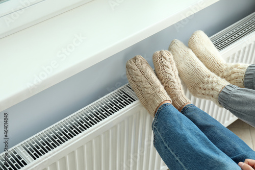 Concept of heating season with legs in knitted boots on radiator photo