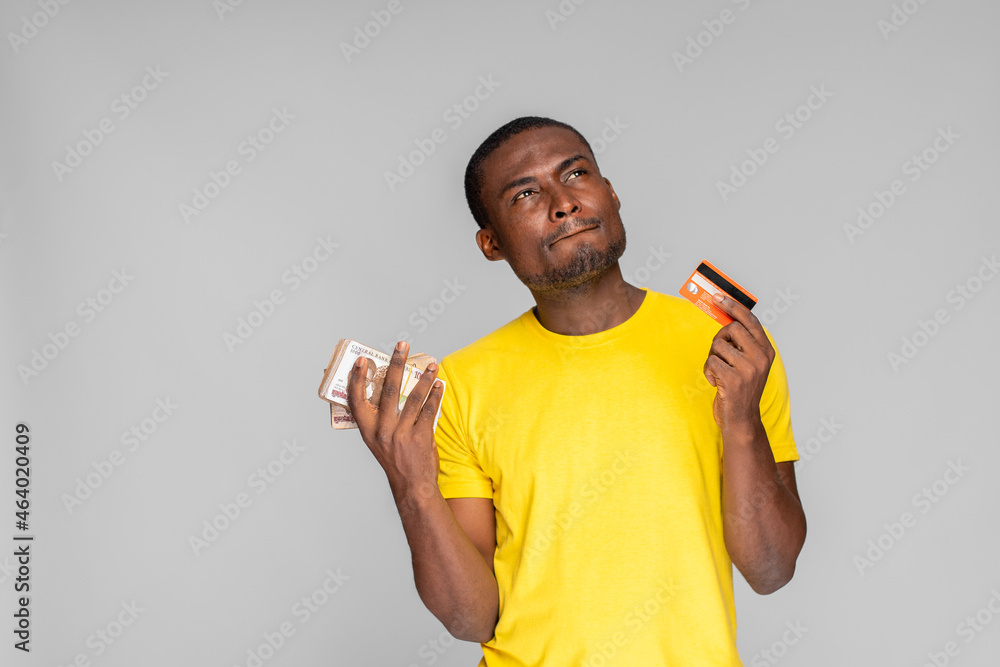 young nigerian man deciding whether to use a credit card or cash young nigerian man deciding whether to use a credit card or cash