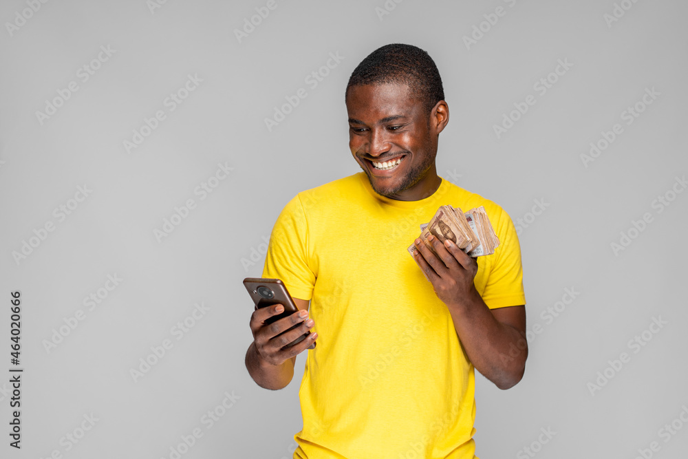excited young nigerian man holding cash and using his phone excited young nigerian man holding cash and using his phone