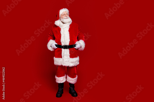 Photo of excited pretty retired man wear santa claus belt boots spectacles walking looking empty space isolated red color background © deagreez