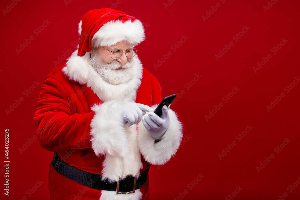 Photo of funny positive retired man wear santa claus costume spectacles typing modern gadget empty space isolated red color background