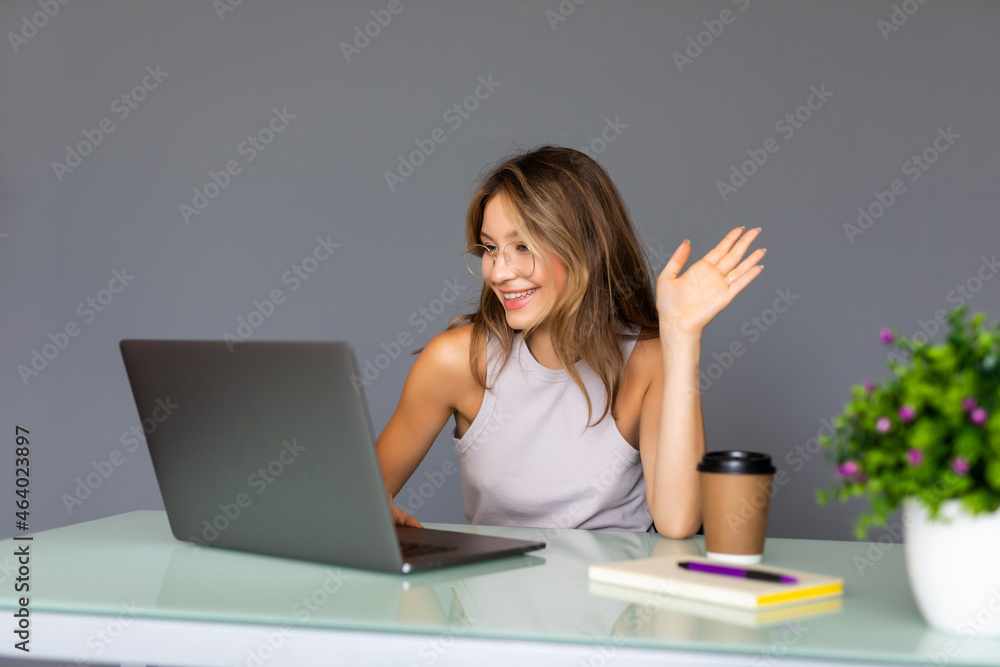 Happy woman waving at her laptop computer as she interacts on a video conferencing call while sitting in an office Happy woman waving at her laptop computer as she interacts on a video conferencing call while sitting in an office