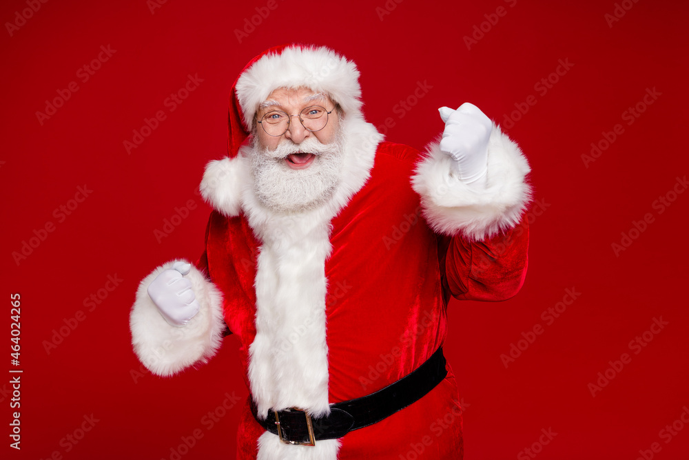 Naklejka premium Photo of impressed lucky man pensioner dressed santa claus costume rising fists smiling isolated red color background