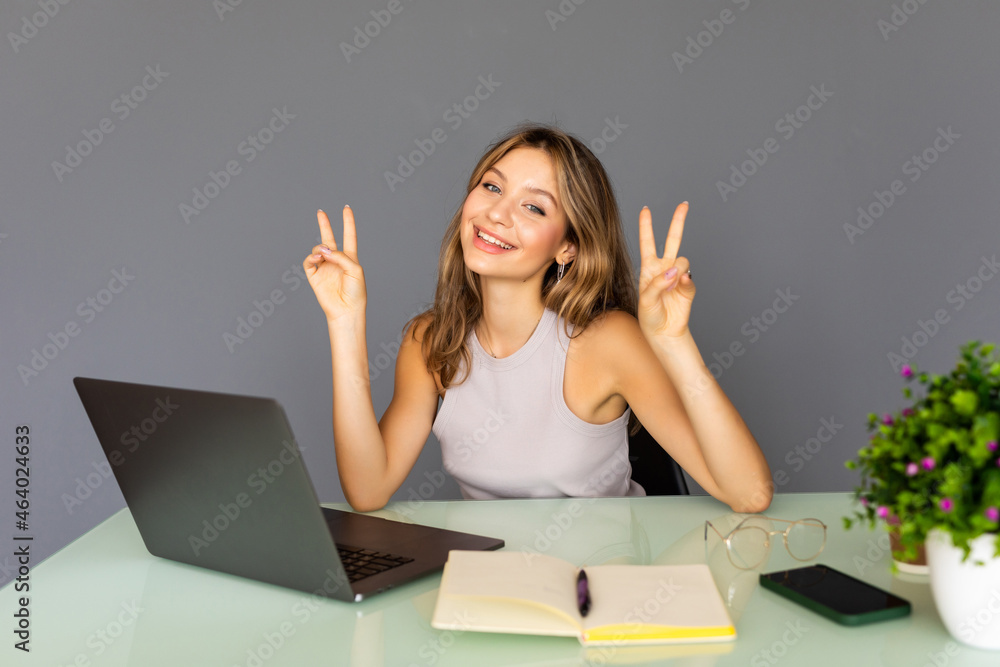 Portrait of happy brunette young woman sitting with victory peace sign in office background. Portrait of happy brunette young woman sitting with victory peace sign in office background.