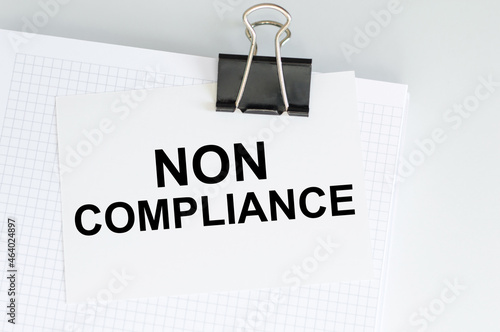 text NON COMPLIANCE in the white short note paper on a clip attached to a white blooncot on the table