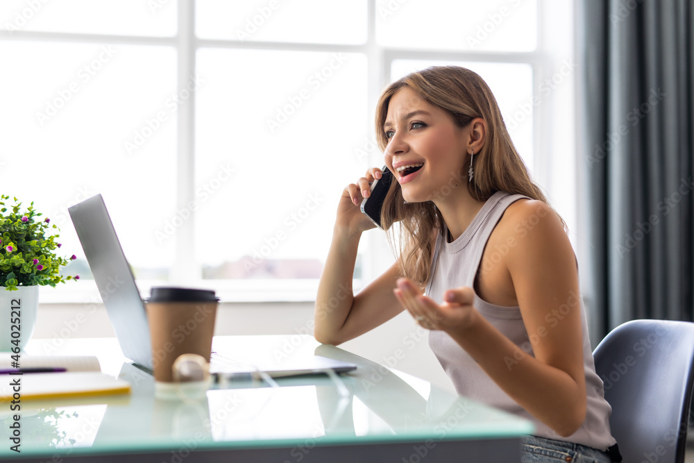 Young business woman sitting at office desk and talking on cell phone