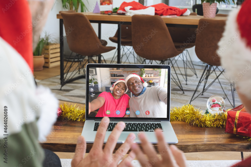 Waving father and daughter making laptop christmas video call with senior african american couple
