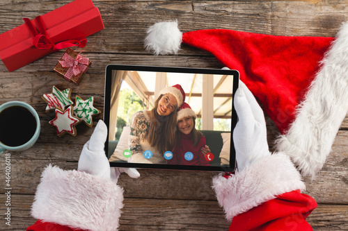 Santa claus holding tablet, making christmas video call with smiling caucasian mother and daughter