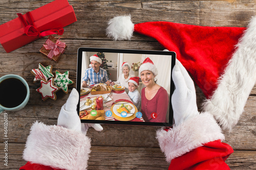 Santa claus holding tablet, making christmas video call with smiling family at dinner table