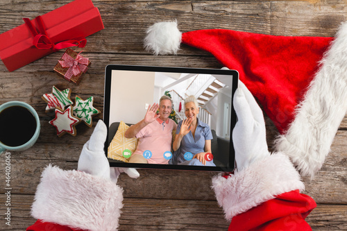 Santa claus making tablet christmas video call with waving senior caucasian couple