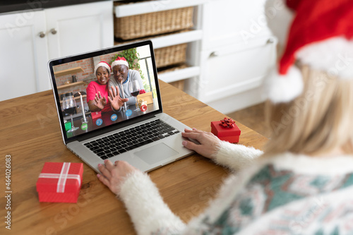 Caucasian woman making laptop christmas video call with waving senior african american couple